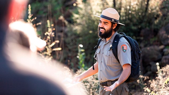 Ranger with backpack smiling with his arms open in the middle of talking.